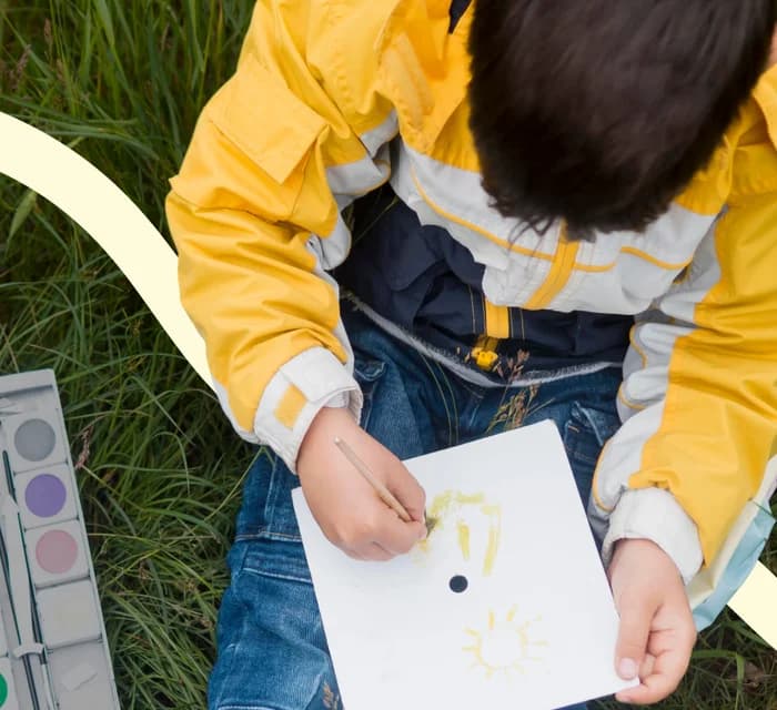 Niño con chaqueta amarilla pintando con acuarelas sobre el césped